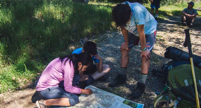 three outward bound students take a break from backpacking to examine a map